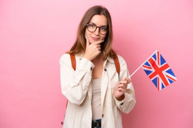 Kafkasyalı genç bir kadın pembe arka planda izole edilmiş bir Birleşik Krallık bayrağı tutuyor.