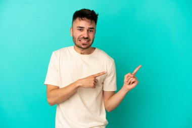 Kafkasyalı genç adam mavi arka planda izole edilmiş korkmuş ve kenarı işaret ediyor.