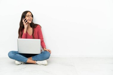 Genç Fransız kız dizüstü bilgisayarıyla yerde oturuyor cep telefonuyla sohbet ediyor.