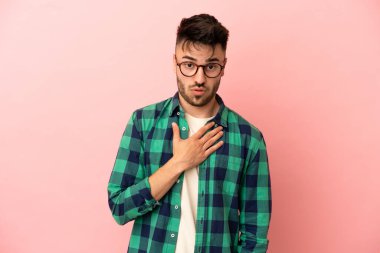 Pembe arka planda izole edilmiş genç beyaz adam sağa bakarken şaşırdı ve şok oldu.