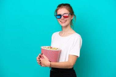 Mavi arka planda 3 boyutlu gözlüklü ve elinde koca bir kova patlamış mısır tutan genç bir İngiliz kadın.