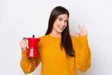 Beyaz arka planda kahve demliği tutan genç Brezilyalı kadın parmaklarıyla işaret veriyor.