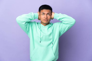Genç Ekvadorlu adam mor arka planda izole edilmiş hayal kırıklığına uğramış ve kulaklarını kapatmış.