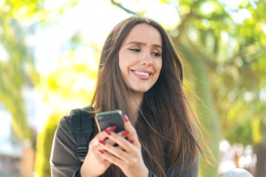 Açık havada cep telefonu kullanan genç bir kadın.