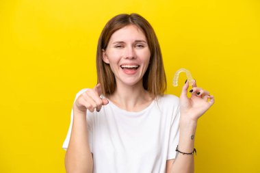 Görünmez diş telleri tutan genç İngiliz kadın şaşırmış ve ön tarafı işaret ediyor.