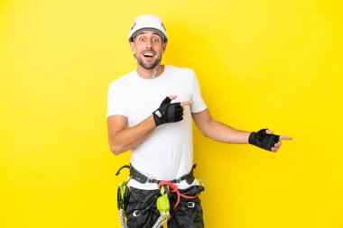 Sarı arka planda izole edilmiş genç kaya tırmanışçısı şaşırmış ve işaret ediyor.