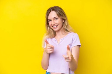 Sarışın İngiliz genç kız. Sarı arka planda izole edilmiş. Önü işaret ediyor ve gülümsüyor.