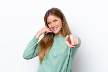 Beyaz arka planda izole edilmiş genç beyaz bir kadın telefon hareketi yapıyor ve ön tarafı işaret ediyor.