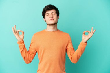 Genç Rus adam Zen pozunda mavi arka planda izole edildi.