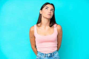 Genç beyaz kadın mavi arka planda izole edilmiş ve yukarı bakıyor.