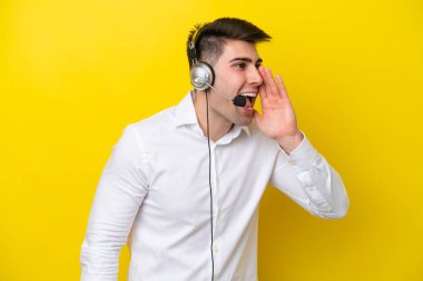 Tele pazarlamacı beyaz adam sarı arka planda izole edilmiş bir kulaklıkla çalışıyor ve ağzı sonuna kadar açık bağırıyor.
