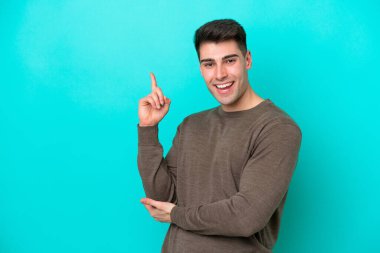 Mavi arka planda izole edilmiş genç beyaz adam mutlu ve dik duruyor.