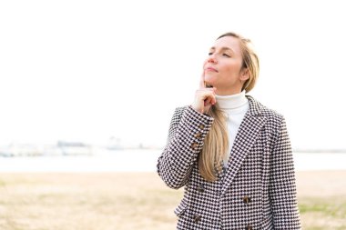 Açık havada genç sarışın bir kadın yukarı bakarken bir fikir düşünüyor.