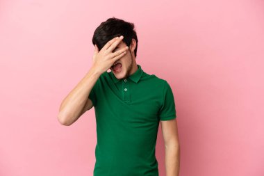 Pembe arka planda izole edilmiş genç bir Rus. Gözleri elleriyle kaplıyor ve gülümsüyor.