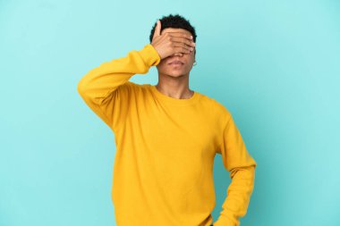 Genç Afro-Amerikalı bir adam mavi arka planda tek başına, gözleri elleriyle kapatıyor. Bir şey görmek istemiyorum.