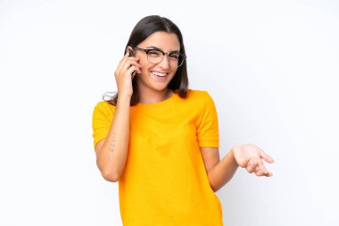 Beyaz arka planda izole edilmiş genç beyaz bir kadın cep telefonuyla sohbet ediyor.