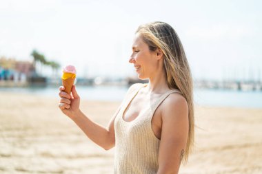 Açık havada kornet dondurmalı genç sarışın kadın, neşeli bir ifadeyle.