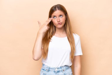 Genç beyaz kadın bej arka planda izole edilmiş ve intihar jesti yapmada sorun yaşıyor.