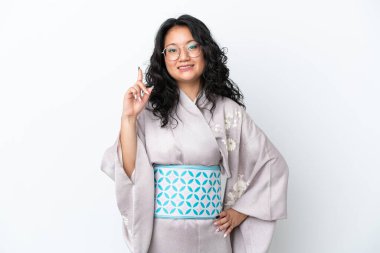 Kimono giyen genç Asyalı kadın beyaz arka planda izole edilmiş ve en iyinin işareti olarak parmağını kaldırıyor.