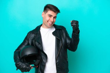 Mavi arka planda izole edilmiş motosiklet kasklı beyaz bir adam zaferi kutluyor.