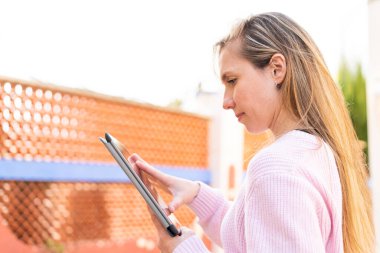 Açık havada elinde tablet tutan genç sarışın kadın.