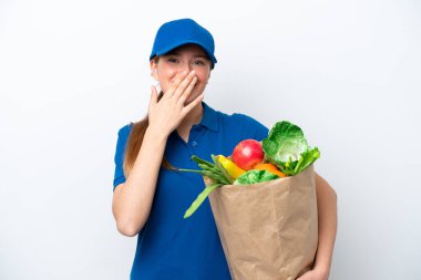 Genç teslimatçı kadın beyaz arka planda izole edilmiş bir paket yiyecek alıyor mutlu ve ağzı eliyle kaplayan bir gülümseme.