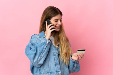 Genç sarışın kadın mavi arka planda izole edilmiş. Kredi kartıyla cep telefonuyla alışveriş yapıyor.