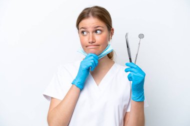 Beyaz arka planda izole edilmiş aletleri tutan beyaz dişçi kadının şüpheleri ve düşünceleri var.