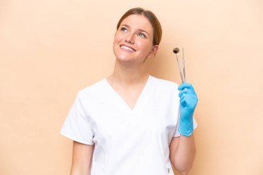 Beyaz dişçi kadının elinde bej arka planda izole edilmiş aletler var.