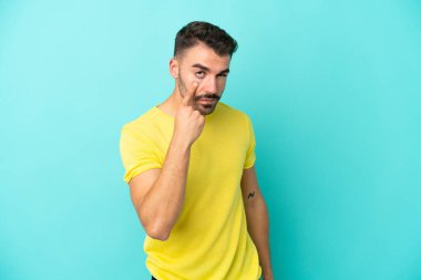 Mavi arka planda izole edilmiş genç beyaz bir adam bir şey gösteriyor.