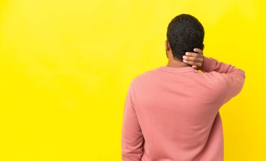 Genç latin adam sarı arka planda izole edilmiş ve düşünüyor.