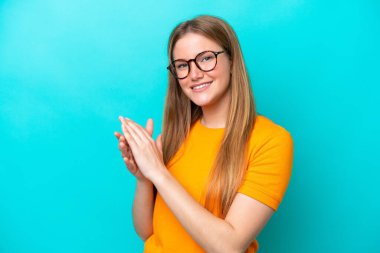 Mavi arka planda izole edilmiş genç beyaz kadın alkışlıyor.