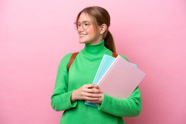 Pembe arka planda izole edilmiş genç beyaz bir kadın. Yan tarafa bakıyor ve gülümsüyor.