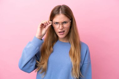 Genç sarışın kadın pembe arka planda izole edilmiş gözlüklü ve sinirli bir ifadeyle