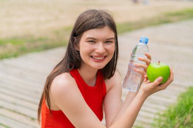 Elmalı ve bir şişe suyla açık havada genç ve güzel bir kadın.