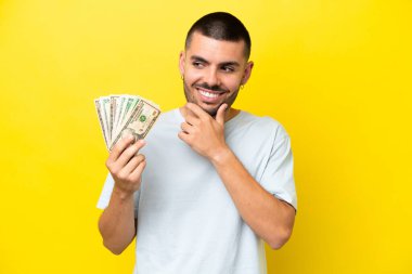 Kafkasyalı genç adam, sarı arka planda izole edilmiş bir şekilde bir sürü para alıyor. Yana bakıyor ve gülümsüyor.