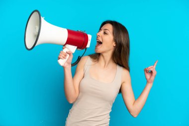 Mavi arka planda izole edilmiş genç beyaz bir kadın megafondan bir şey duyurmak için bağırıyor.