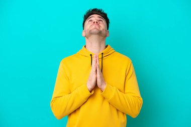 Mavi arka planda izole edilmiş genç beyaz adam avuç içlerini bir arada tutuyor. İnsan bir şey ister.