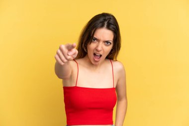 Sarı arka planda izole edilmiş genç beyaz kadın hayal kırıklığına uğramış ve ön tarafı işaret ediyor.