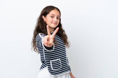 Beyaz arka planda izole edilmiş küçük beyaz kız gülümsüyor ve zafer işareti gösteriyor.
