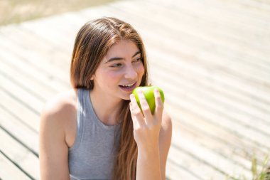 Genç, güzel, beyaz bir kadın elinde mutlu bir ifadeyle bir elma tutuyor.