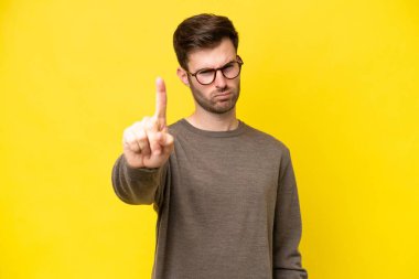 Sarı arka planda izole edilmiş beyaz bir adam ciddi bir ifadeye sahip birini sayıyor.