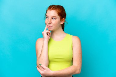 Kırmızımsı genç kadın mavi arka planda izole edilmiş, yukarı bakarken şüpheleri var.