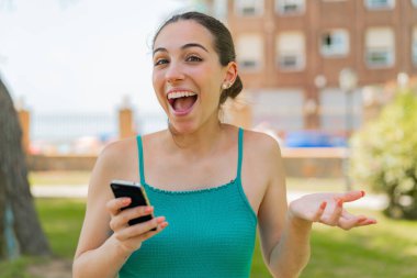 Dışarıda cep telefonu kullanan genç ve güzel bir kadın şok olmuş bir yüz ifadesi var.