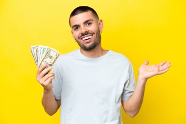 Kafkasyalı genç adam, sarı arka planda izole edilmiş ve şok olmuş bir yüz ifadesiyle bir sürü para alıyor.
