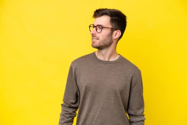 Sarı arka planda izole edilmiş genç beyaz adam yana bakıyor ve gülümsüyor.