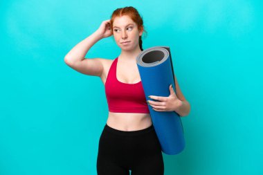 Genç spor kırmızısı kadın yoga derslerine giderken elinde mavi arka planda bir minder tutarken kuşkuları vardı.