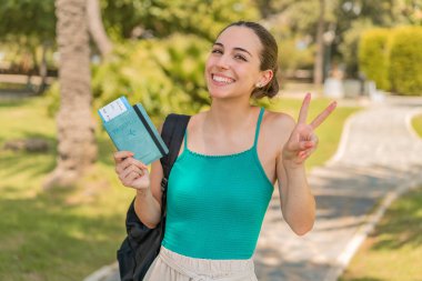 Dışarıda pasaportu olan genç ve güzel bir kadın gülümsüyor ve zafer işareti gösteriyor.