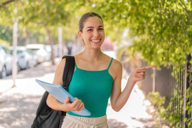 Açık havada genç ve güzel bir bayan bir ürün sunmak için kenarı işaret ediyor.