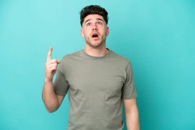 Mavi arka planda izole edilmiş genç beyaz adam yukarı bakıyor ve şaşırıyor.